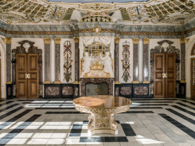 Salen i det lille jagtslot, Eremitagen, i Jægersborg Dyrehave. Opført og indrettet i prægtig barokstil i 1730’erne for Christian den 6. (1699‑1746) og familie. Spisesalens udsmykning rum‑ mer både ægte marmor anvendt som dørindfatninger samt stukmarmor til søjler og pilastre. Væggenes brystpaneler i fyrretræ er marmorerede, så det imiterer rummets ægte mar‑ mor. Foto: Roberto Fortuna.